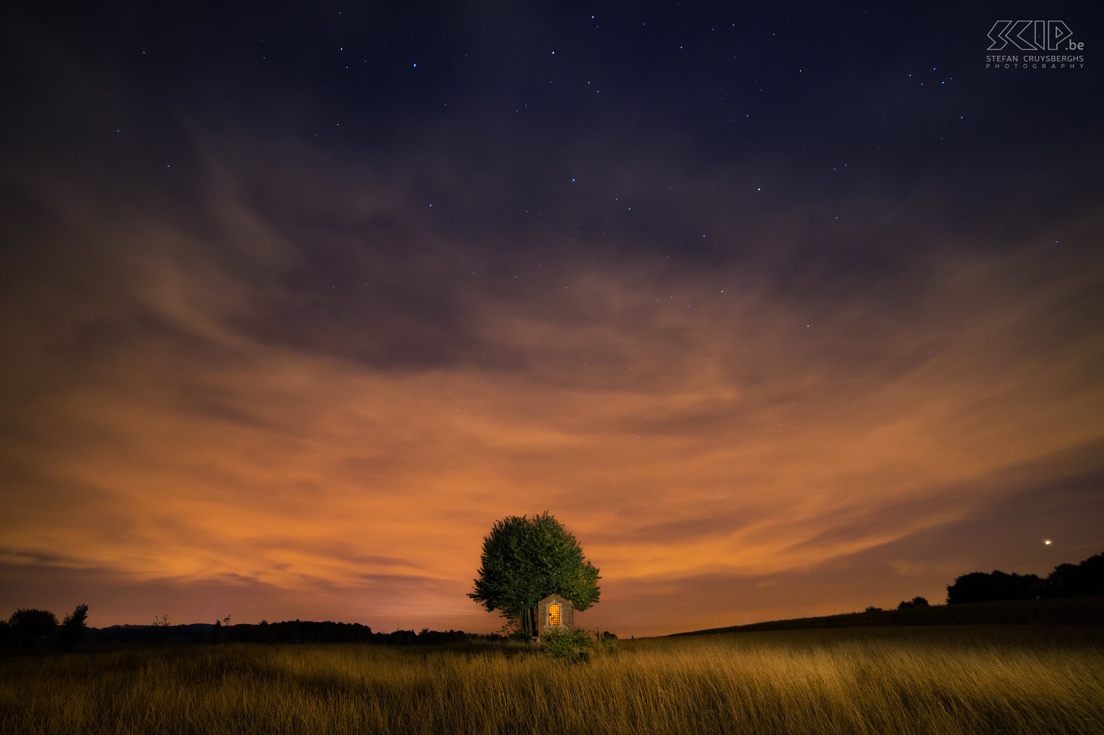 Hageland by night - Saint Joseph chapel The picturesque Sint-Jozef chapel in Sint-Pieters-Rode (Holsbeek) is one of my favorite spots. This photo was made in August and I used strong lamps to illuminate the chapel and the field. The orange clouds are created by the reflection of the street lighting. Stefan Cruysberghs